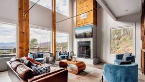Ein modernes Wohnzimmer mit Kamin, großen Fenstern und Blick ins Freie.