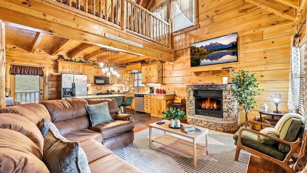 A log cabin interior with a living room, kitchen, dining area, and a stone fireplace. - Relaxing Cabin-Hot Tub-Game Room-Large outdoors (Sevierville)