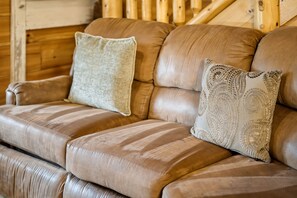 Eine braune Ledersofa mit zwei dekorativen Kissen, eine Holzwand und eine Treppe im Hintergrund.