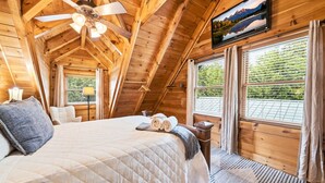 A wooden cabin bedroom with a bed, ceiling fan, windows, and a TV. - Relaxing Cabin-Hot Tub-Game Room-Large outdoors (Sevierville)