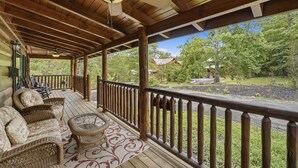 A wooden deck with wicker furniture, a ceiling fan, and a view of a forested area. - Relaxing Cabin-Hot Tub-Game Room-Large outdoors (Sevierville)
