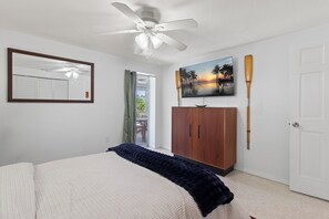 Ein Schlafzimmer mit Bett, Deckenventilator, Kleiderschrank, einem Gemälde und einer Tür.