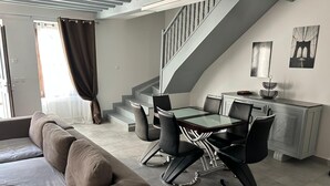 Een moderne woonkamer met een bank, eettafel, stoelen, een trap en kunst aan de muur.