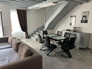 A modern living room with a sofa, dining table, chairs, staircase, and artwork on the wall. - A lovely, spacious, quiet house with a charming little yard (Dampierre-sous-Bouhy)