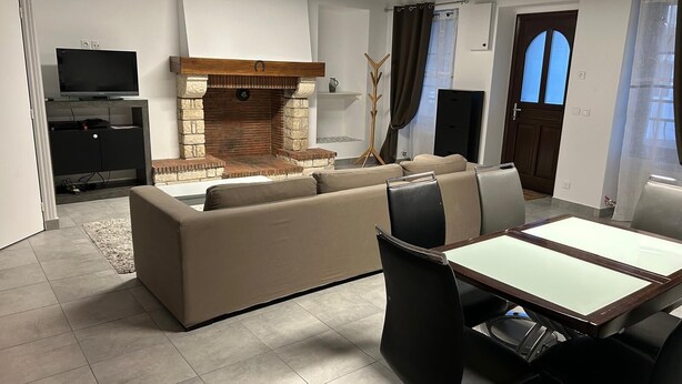 Een moderne woonkamer met een bank, een eettafel met stoelen, een open haard, een televisie en een deur met een raam.