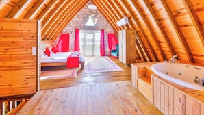 A wooden interior with a sloped ceiling, a bed, a bathroom with a bathtub, and a stone wall. - Serene Bungalow Retreat With Private Pool in Kaş, Türkiye (Kaş)
