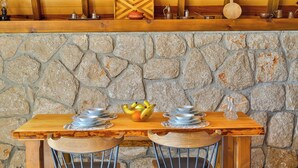 A rustic wooden table with metal serving dishes and a fruit bowl, set against a stone wall with wooden beams above. - Serene Bungalow Retreat With Private Pool in Kaş, Türkiye (Kaş)