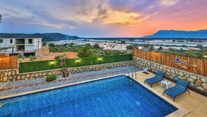 A swimming pool with lounge chairs, a wooden fence, and a view of a cityscape and mountains. - Serene Bungalow Retreat With Private Pool in Kaş, Türkiye (Kaş)