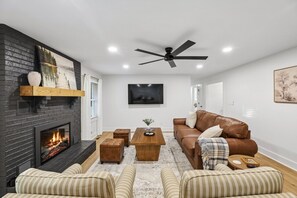 Ein Wohnzimmer mit Kamin, einem braunen Ledersofa, einem Holztisch und gestreiften Sesseln.