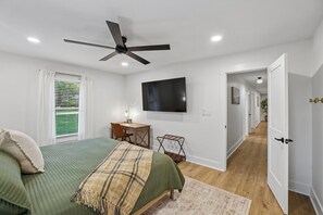Ein Schlafzimmer mit Bett, Schreibtisch, Stuhl, Fernseher und Deckenventilator.