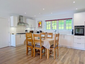 Una cocina moderna con armarios blancos, una mesa de comedor con sillas de madera, una estufa a gas y una ventana con vistas al verdor.