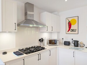 Una cocina moderna con armarios blancos, una campana extractora de acero inoxidable, una estufa a gas, un microondas y un hervidor.