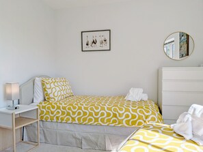 Un dormitorio con una cama, mesita de noche, lámpara, cómoda, un cuadro enmarcado y un espejo.
