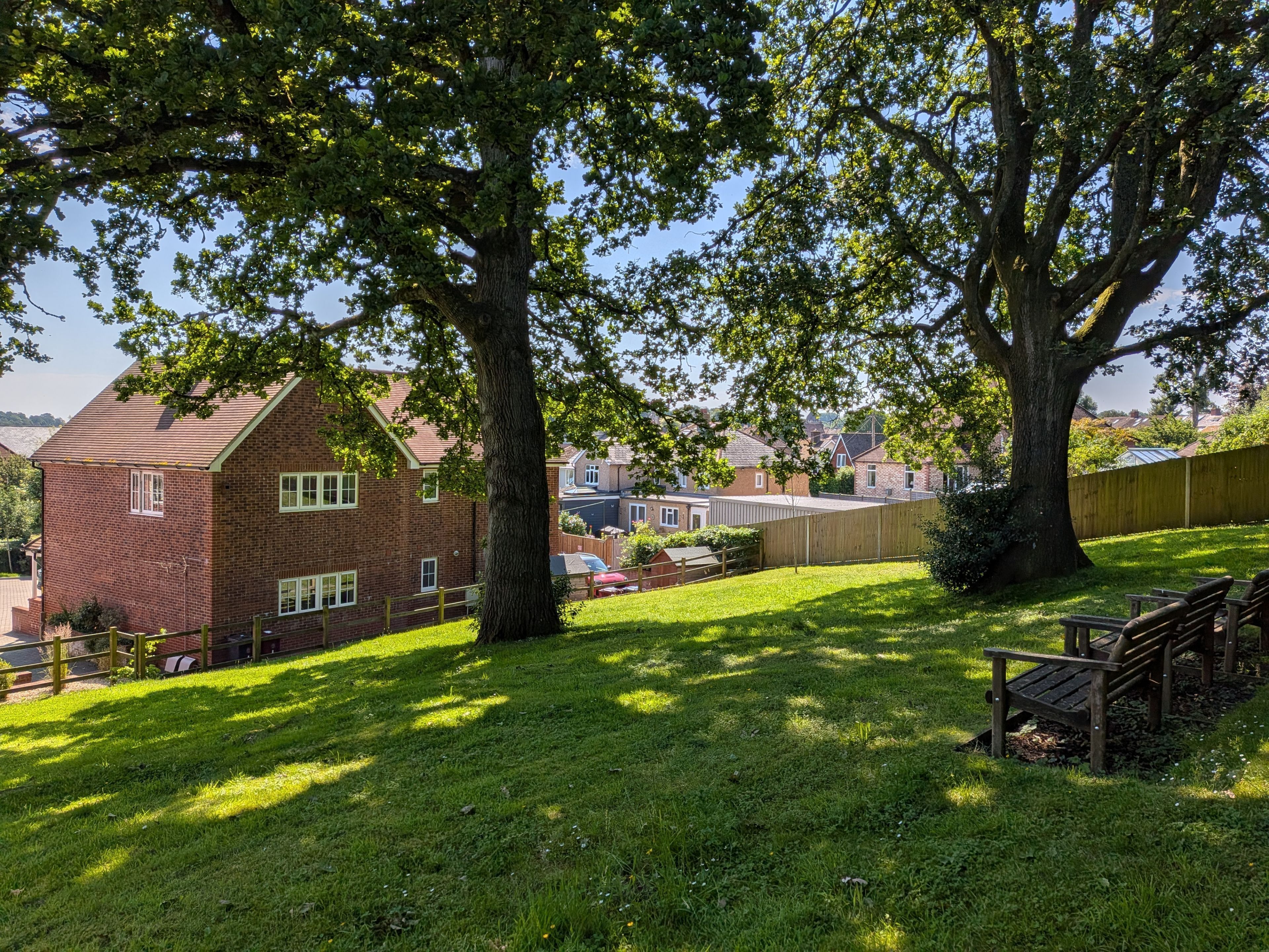 A residential area with a brick house, a large tree, and a grassy lawn.
