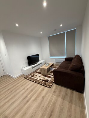 Ein modernes Wohnzimmer mit einem Flachbildfernseher, einem braunen Sofa, einem Holztisch und einem gemusterten Teppich.
