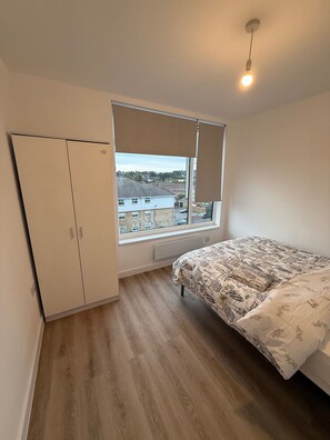 Ein Schlafzimmer mit Bett, Schrank, Fenster mit Jalousien und einer Pendelleuchte.