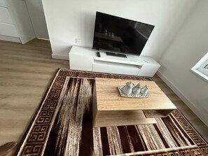 Ein modernes Wohnzimmer mit Flachbildfernseher, Couchtisch aus Holz und einem gemusterten Teppich.