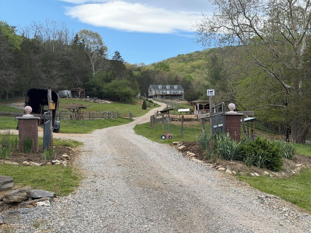 A gravel driveway leading to a house with a fenced yard, a mailbox, and a signpost.