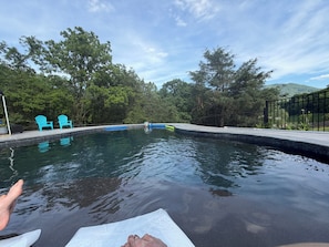 Piscina con sillas azules, rodeada de árboles y una valla.