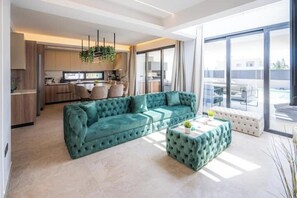 Una sala de estar moderna con un sofá color turquesa, una mesa de centro y una cocina al fondo.