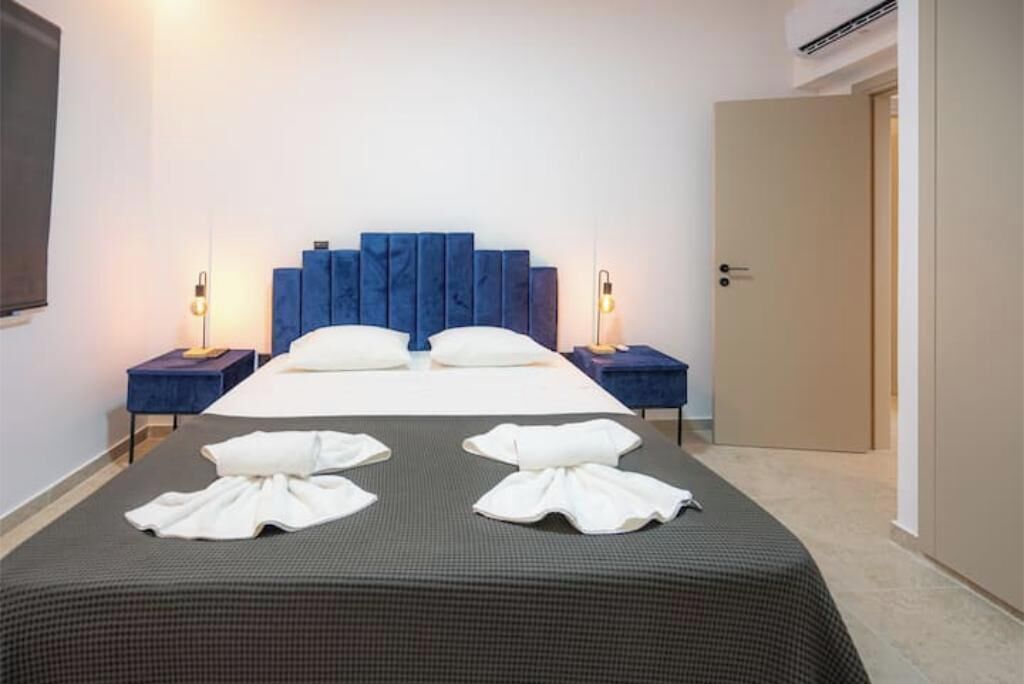 Habitación de hotel con una cama, dos mesitas de noche, una puerta y un televisor montado en la pared.