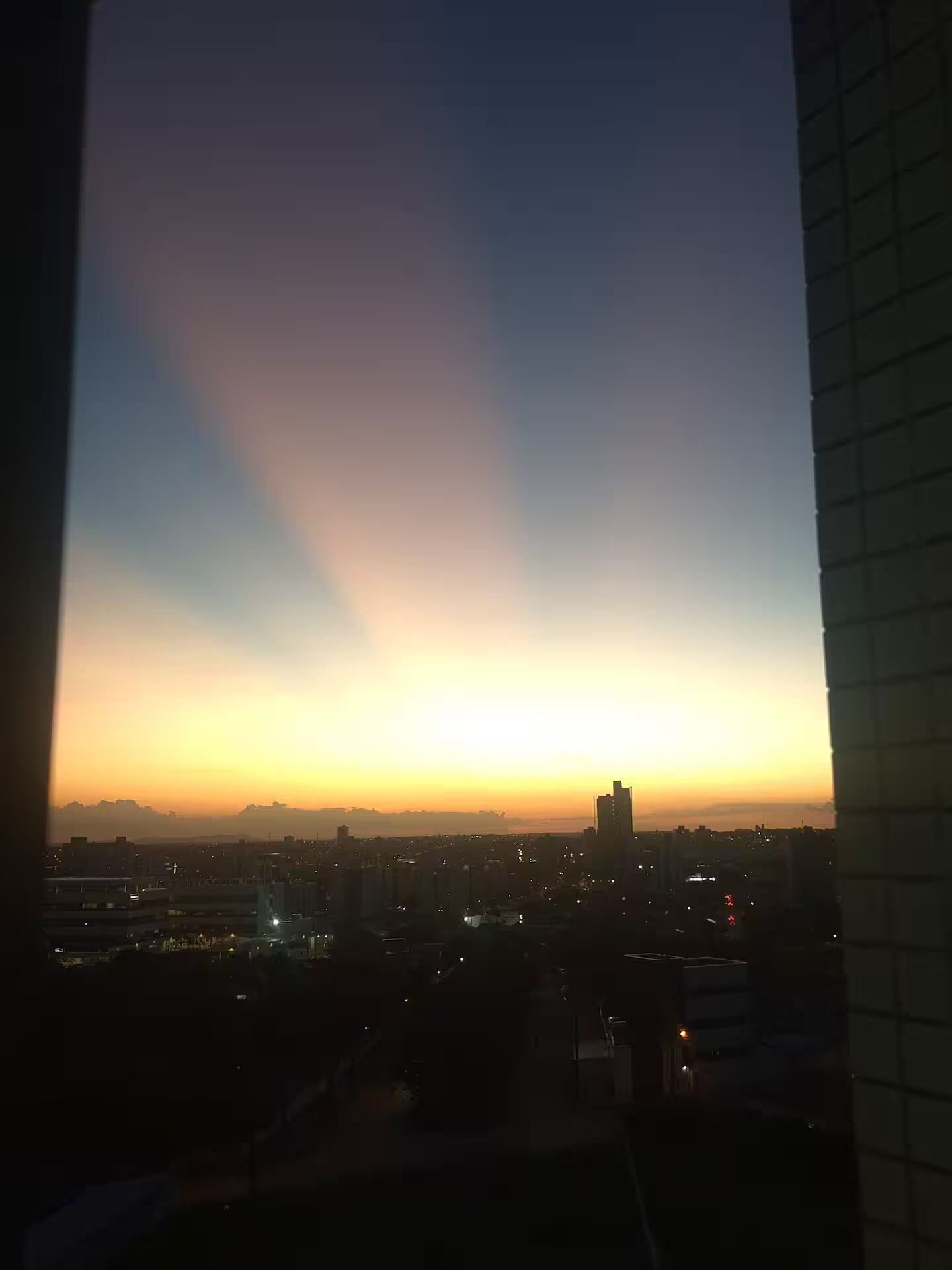 A cityscape at dusk with buildings silhouetted against a sky with a gradient from yellow to blue.