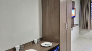 Un coin repas avec une table en bois, deux chaises bleues, un téléviseur fixé au mur et une armoire.