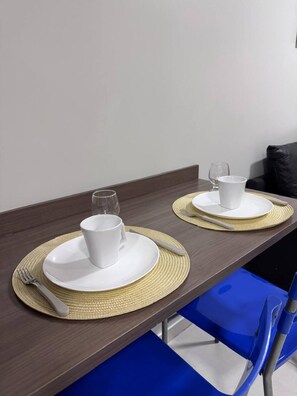 Une table à manger avec deux assiettes blanches, chacune accompagnée d’une tasse et d’un verre, et sur laquelle sont posés une fourchette et un couteau.