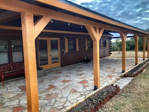 A covered patio area with a stone floor, wooden beams, and a bench. - Side by Side Cabins on a Texas Ranch, Perfect for a Family Glamping Getaway from San Antonio (Mico)