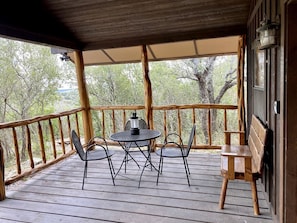 A covered outdoor area with a table and chairs, a lantern, and a wooden bench. - Side by Side Cabins on a Texas Ranch, Perfect for a Family Glamping Getaway from San Antonio (Mico)