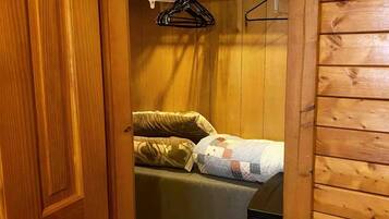 A wooden-paneled room with a bed, a hanging clothes rack, and a door.