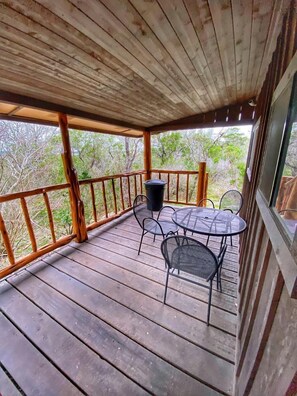 Una terraza de madera con una mesa y sillas, un bote de basura y vistas a árboles.