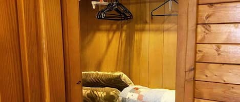 Una habitación con paneles de madera, una cama, un perchero y una puerta.