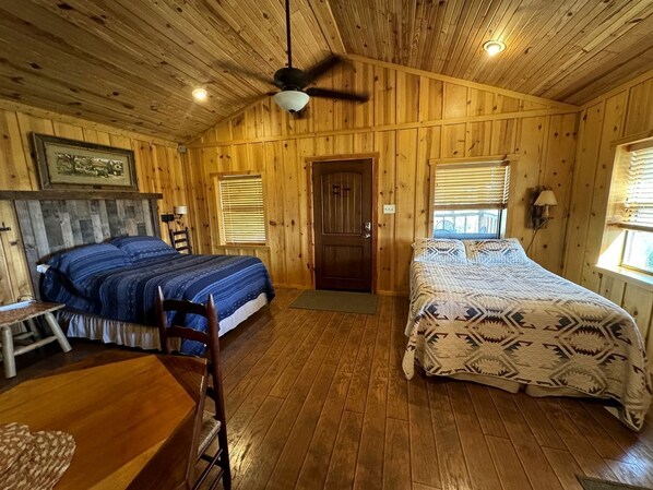 A wooden cabin with two beds, a dining table, and a ceiling fan.
