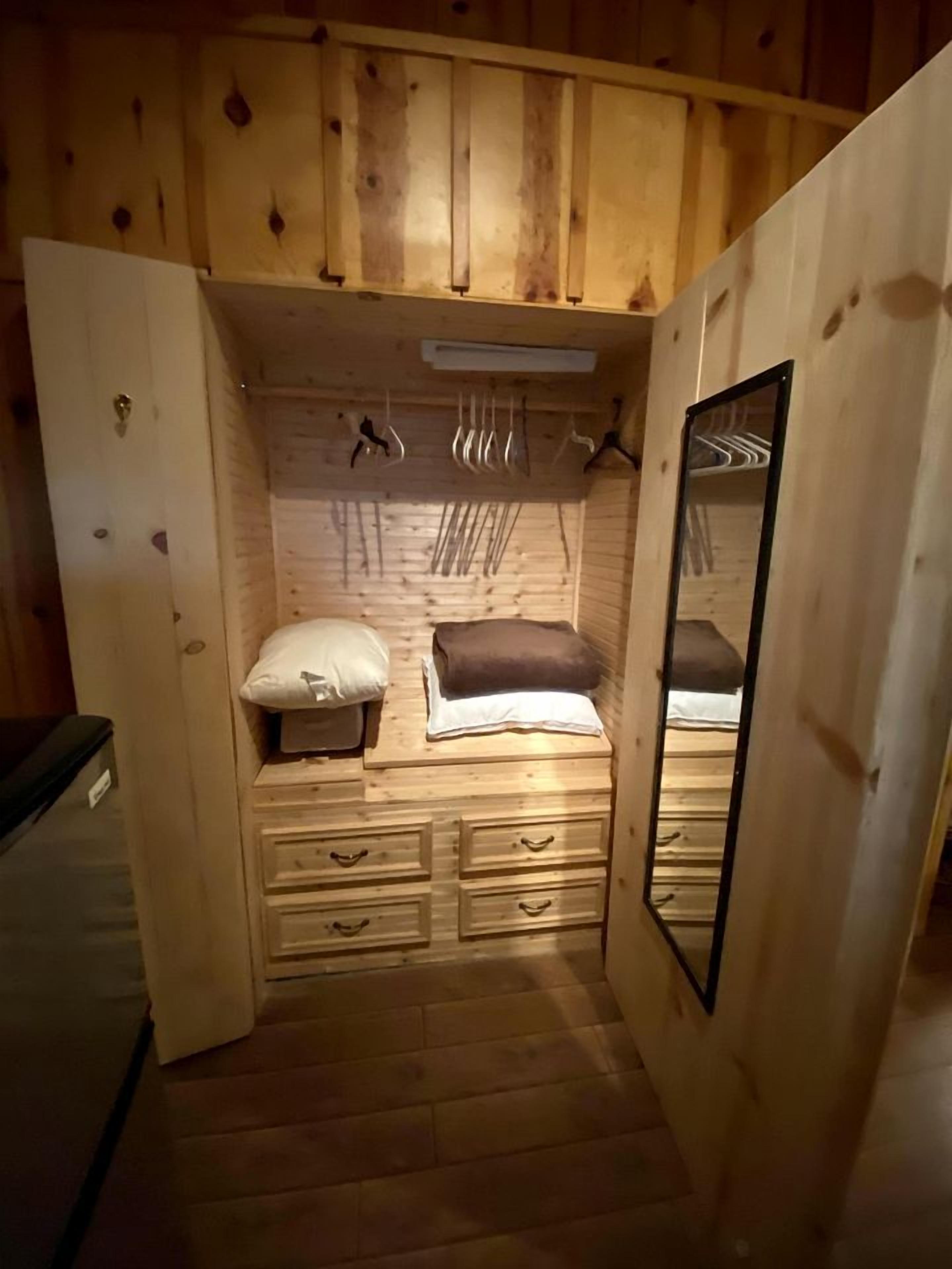 Una habitación pequeña de madera con una cama, un tocador, un espejo y un perchero.