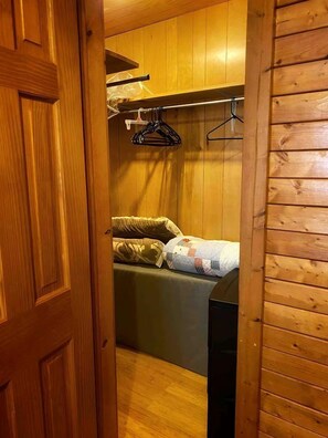 A wooden-paneled room with a bed, a hanging clothes rack, and a door.