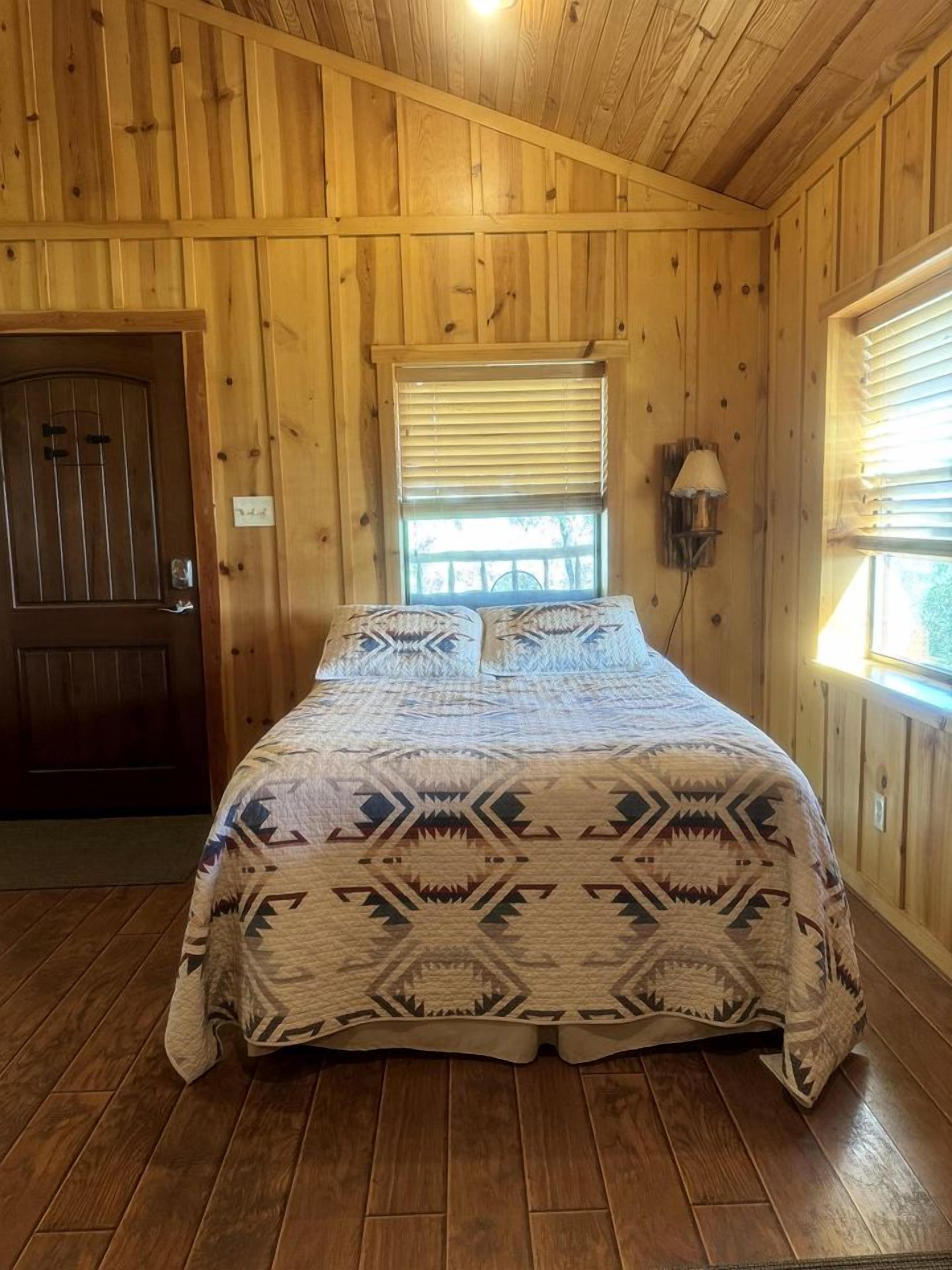 A wooden-paneled room with a bed, a door, and a window with blinds.