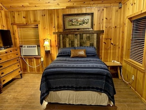 A wooden-paneled room with a bed, dresser, television, and heater. - Side by Side Cabins on a Texas Ranch, Perfect for a Family Glamping Getaway from San Antonio (Mico)