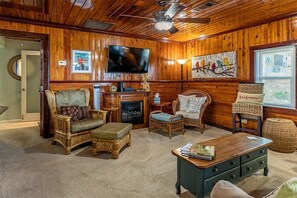 Una sala de estar acogedora con chimenea, muebles de mimbre, un televisor y un cuadro en la pared.