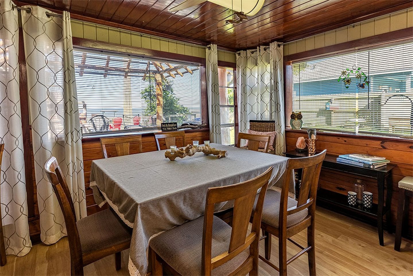 Un comedor con una mesa dispuesta para cuatro, sillas de madera, un banco y vistas al exterior.