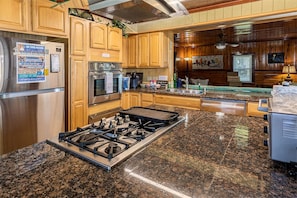 Una cocina con encimeras de granito, electrodomésticos de acero inoxidable, armarios de madera, estufa a gas y horno empotrado.