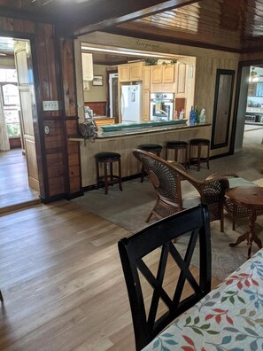 A wooden interior with a kitchen area, bar stools, and a dining table. - Vintage-Inspired Haven with Bright Interiors & Relaxing Outdoor Spaces in Bacliff, Texas (Bacliff)