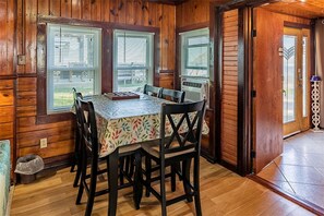 Ein Interieur einer Holzhütte mit Esstisch, Stühlen und einem Fenster mit Jalousien.