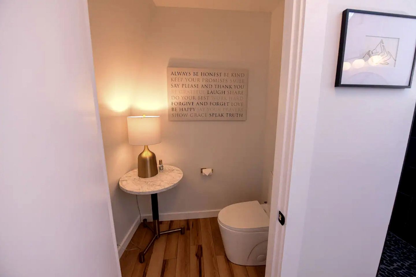 A small bathroom with a toilet, a vanity with a lamp, and a motivational quote on the wall.