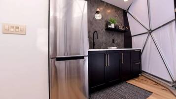 A modern kitchen with a stainless steel refrigerator, black cabinets, a white countertop, and a hanging pendant light.