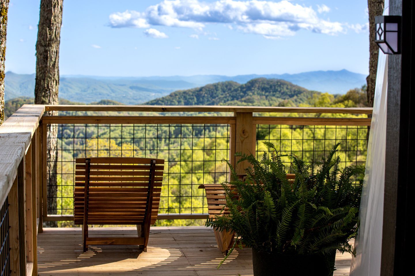 Una terraza de madera con un banco y una planta en maceta, con vistas a un paisaje montañoso.