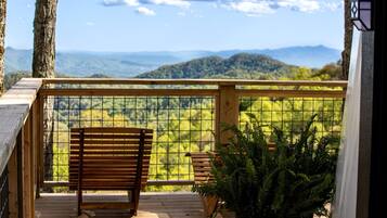 Una terraza de madera con un banco y una planta en maceta, con vistas a un paisaje montañoso.