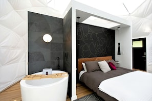 Un dormitorio moderno con una cama grande, un espejo redondo y un inodoro blanco.