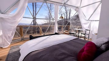 A spacious room with a large bed, a small table, and a chair, all under a geometric glass ceiling with a view of the outdoors.