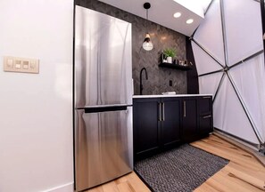 Eine moderne Küche mit einem Edelstahl-Kühlschrank, schwarzen Schränken, einer weißen Arbeitsplatte und einer hängenden Pendelleuchte.